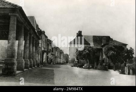 Villefranche du Perigord, Dordogne Frankreich. Diese Postkarte zeigt eine Straßenszene mit Blick auf das Denkmal der Stadt. Villefranche-du-Perigord ist eine Bastidstadt, die 1261 von Alphonse de Poitiers gegründet wurde. Die Stadt hat sich um ihren zentralen Platz, den „La Place de la Halle“, mit ihrer traditionellen, offenen Markthalle aufgebaut, die auf der linken Seite zu sehen ist. Stockfoto