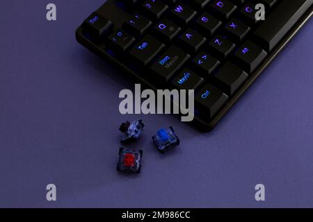 Mechanische RGB-Tastatur für Gamer auf einem Schreibtisch mit violettem Licht und seitlichen Schaltern. Stockfoto