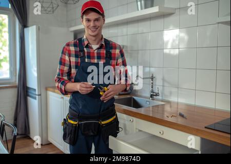 Lächelnder Servicemann mit Zange und Passstift in den Händen, der an einer offenen Schrankschublade steht Stockfoto