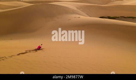 Frau sitzt in Sanddünen in der Wüste und fotografiert bei Sonnenuntergang, Maspalomas, Gran Canaria, Kanarische Inseln, Spanien Stockfoto