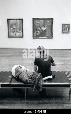 Besucher ruhen sich auf einer Bank in der Tate Gallery, London, England. Stockfoto