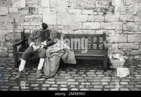 Ein Paar in historischen Kostümen, das auf einer Bank in einem gepflasterten Innenhof schläft. Stockfoto