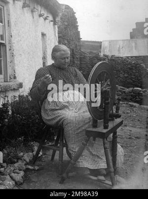 Frau vor ihrem Haus, die Wolle in Glen Columbkille (Glencolmcille, Gleann Cholm Cille), County Donegal, Nordwesten Irlands spinnt. Stockfoto