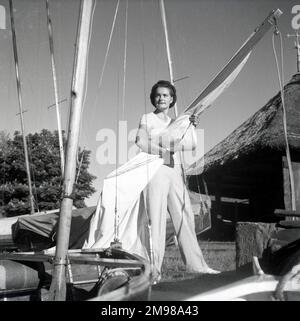 Barbara Hepworth (1903-1975), englische Künstlerin und Bildhauerin, steht neben einer Yacht, mit einem strohgedeckten Cottage auf der rechten Seite. Stockfoto