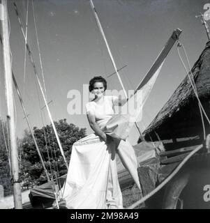 Barbara Hepworth (1903-1975), englische Künstlerin und Bildhauerin, die das Segel einer Yacht hält, mit einem strohgedeckten Häuschen auf der rechten Seite. Stockfoto