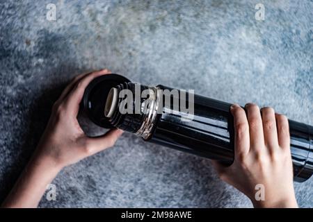 Draufsicht einer Person, die ein warmes Getränk aus einem Thermoskolben ausschüttet Stockfoto