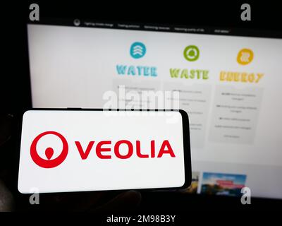 Person, die ein Mobiltelefon mit dem Logo des französischen Unternehmens Veolia Environnement SA auf dem Bildschirm vor der Unternehmenswebseite hält. Konzentrieren Sie sich auf das Display des Telefons. Stockfoto