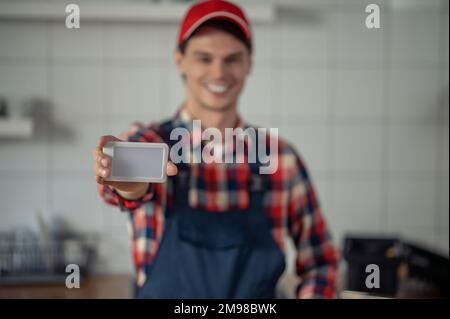 Hüftporträt eines lächelnden Elektrikers, der eine neue Lichtschalterplatte vor der Kamera vorführt Stockfoto