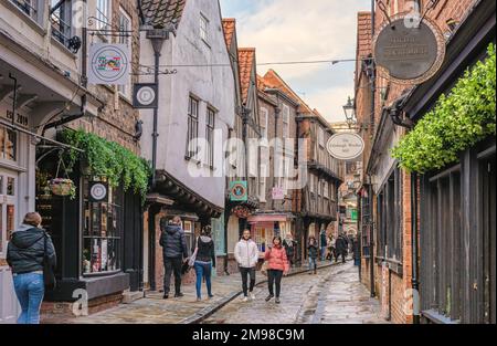 Die malerischen und historischen Shambles in York. Geschäfte säumen die malerische und historische Straße, während Touristen zu Fuß unterwegs sind. Ein Himmel mit Wolken ist oben. Stockfoto