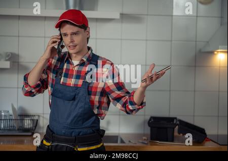 Taillenhochgezogenes Porträt eines ernsthaften Mechanikers, der etwas auf dem Handy in der Kundenküche diskutiert Stockfoto