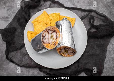 Mexikanischer Rindfleischburrito auf einem kleinen Teller mit Chips Nachos Stockfoto