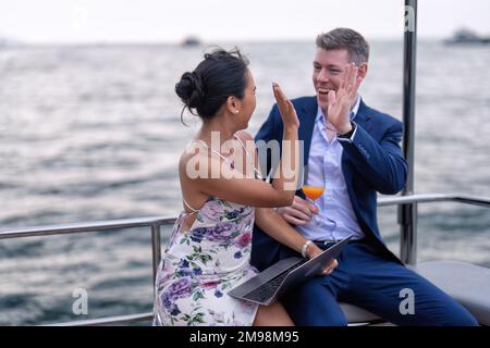 Geschäftsmann und Freundin im Urlaub, die auf der Yacht segeln, schauen Sie auf dem Laptop nach und erhalten Sie gute Nachrichten Stockfoto