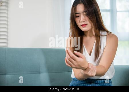 Asiatische junge Frau sitzt auf dem Sofa hält leiden ihr Handgelenk zu Hause Stockfoto