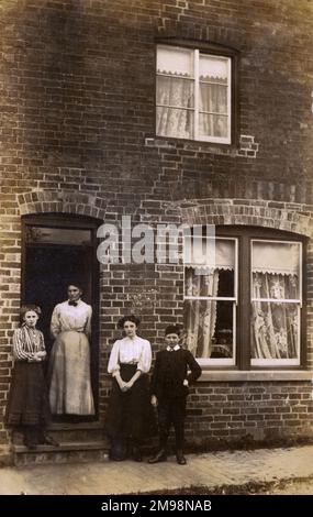 Foto der Schwelle - Edwardianische Familie (auf dem Weg nach oben - sie haben gerade den Ziegelstein neu ausgerichtet und ein paar neue Spitzenvorhänge eingebaut!) Vor ihrem terrassenförmigen Heim Stockfoto