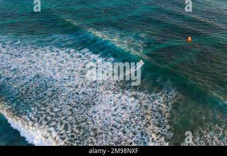 Luftaufnahme über der Bucht des blauen Korallenriffs, breite Wellen mit Kiteboarder auf orangefarbenen Power Drachen. Aktive Sportler und Schönheit im Naturkonzept Aerial vid Stockfoto