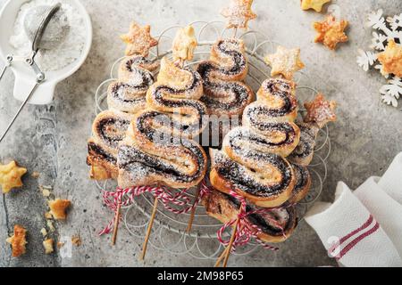 Weihnachtsbaumförmige Blätterkuchen mit Schokoladenfüllung, Zuckerpulver und Lutscher auf altem, weißem Holzhintergrund. Weihnachten, Neujahr, Appetit Stockfoto