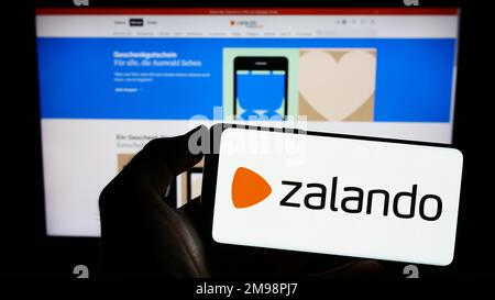 Person, die ein Smartphone mit dem Logo des deutschen E-Commerce-Unternehmens Zalando SE auf dem Bildschirm vor der Website hält. Konzentrieren Sie sich auf das Display des Telefons. Stockfoto