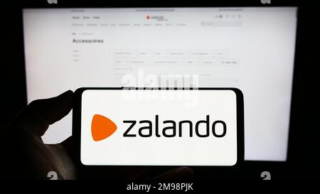 Person, die ein Mobiltelefon mit dem Logo des deutschen E-Commerce-Unternehmens Zalando SE auf dem Bildschirm vor der geschäftlichen Webseite hält. Konzentrieren Sie sich auf das Display des Telefons. Stockfoto