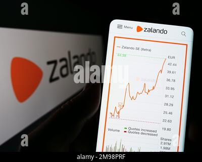 Person, die ein Mobiltelefon mit einer Webseite des deutschen E-Commerce-Unternehmens Zalando SE auf dem Bildschirm vor dem Logo hält. Konzentrieren Sie sich auf die Mitte des Telefondisplays. Stockfoto