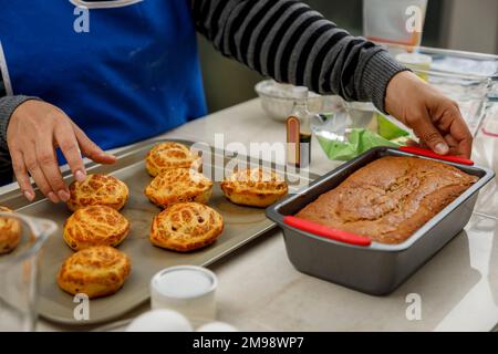 Frauenhände, die das Brot und die Zimtschnecken arrangieren, die sie gerade zu Hause gebacken hat Stockfoto