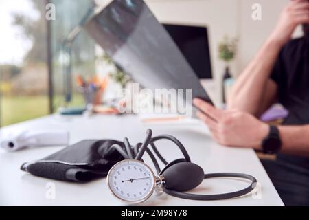 Nahaufnahme eines männlichen Arztes am Schreibtisch mit CT- oder MRT-Scan und Blutdrucksphygmomanometer Stockfoto