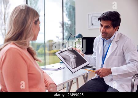 Arzt trägt weißen Kittel im Büro mit einer älteren Patientin, die auf medizinisches Röntgen oder Scannen schaut Stockfoto