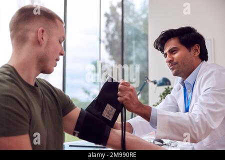 Männlicher Arzt oder Hausarzt junger männlicher Patient, der mit Sphygmomanometer Blutdruck nimmt Stockfoto