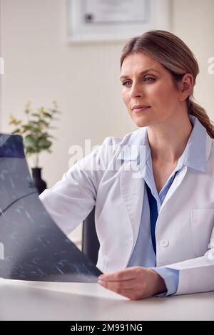 Ärztin oder Allgemeinärztin mit weißem Mantel sitzt am Schreibtisch im Büro und schaut sich CT- oder MRT-Scan an Stockfoto