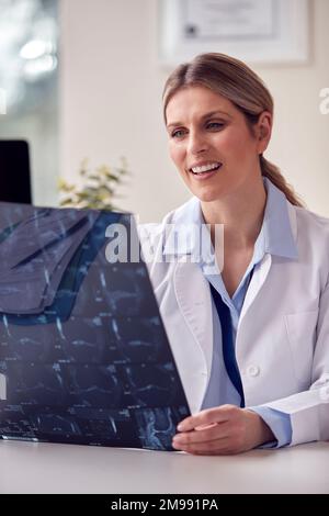 Ärztin oder Allgemeinärztin mit weißem Mantel sitzt am Schreibtisch im Büro und schaut sich CT- oder MRT-Scan an Stockfoto