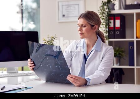 Ärztin oder Allgemeinärztin mit weißem Mantel sitzt am Schreibtisch im Büro und schaut sich CT- oder MRT-Scan an Stockfoto