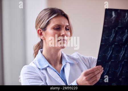 Weibliche Ärztin trägt weißen Kittel steht im Krankenhauskorridor und sieht sich CT oder MRT an Stockfoto
