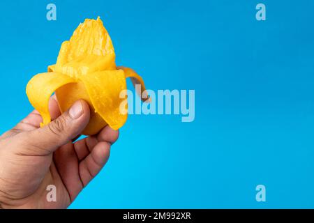 Hand mit einer geschälten manila-Mango, blauer Hintergrund und Kopierraum Stockfoto