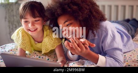 Mädchen Und Junge Im Schlafzimmer Liegen Auf Dem Bett Und Benutzen Ein Digitales Tablet Zusammen Stockfoto