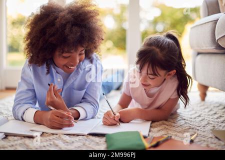 Junge Und Mädchen, Die In Der Lounge Zu Hause Auf Dem Teppich Liegen Und Zusammen Hausaufgaben Machen Stockfoto