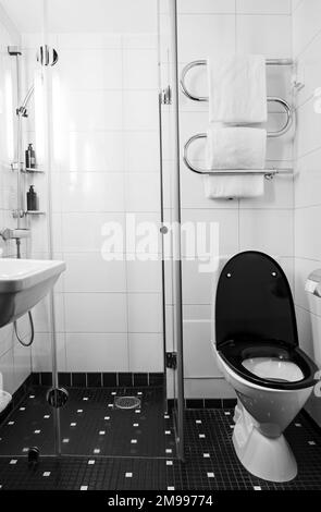 Modernes, kleines Hotelbad mit Glasdusche und schwarz-weißem Nahbild Stockfoto