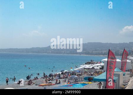 Ein Bild eines bevölkerten Strands an der Küste der Cote d'azur in frankreich mit einem wunderschönen blauen Himmel und einem Hügel im Hintergrund. Stockfoto