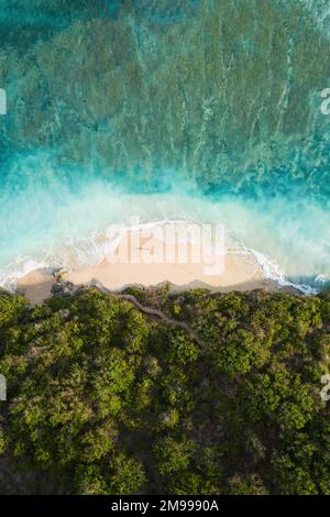 Blick von oben, atemberaubender Blick auf eine Person, die an einem wunderschönen Strand wackelt, umgeben von einem türkisfarbenen rauen Meer bei Sonnenuntergang, Green Bowl Beach, Südbali Stockfoto