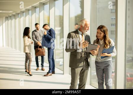 Attraktiver Geschäftsmann mit seiner jungen Frau Coleague, der im Büro ein digitales Tablet benutzt Stockfoto