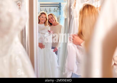 Mutter, Die Der Erwachsenen Tochter Bei Der Auswahl Des Hochzeitskleids Im Brautgeschäft Hilft Stockfoto