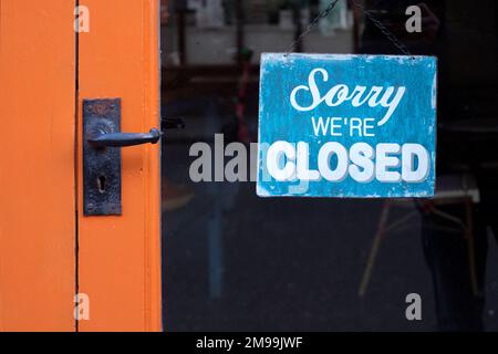 Ein Schild mit der Aufschrift „Sorry we're Closed“ ist deutlich an einem Fenster der Ladentür angebracht. Stockfoto