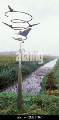 Die Landebahn hier, im alten Vorland der Maas in Keent, wurde von den Deutschen als Notlandeplatz gebaut, aber nie von ihnen genutzt. Am 26. September 1944 landete jedoch 209 C47 Dakotas vom 52. Wing-Truppen-Trägerkommando in Keent mit Truppen und Vorräten für die Amerikaner und die 2. Britische Armee. Trotz des marschigen und feuchten Bodens wurde der Streifen weiterhin von Kampfgeschwadern der taktischen Luftwaffe 2. genutzt. Das unverwechselbare Denkmal, das Flugzeuge zeigt, die von einer Spiralfeder fliegen, als ob sie um die Landebahn kreisen, wurde von Albert Sanders entworfen. Rechts neben dem Metall M Stockfoto