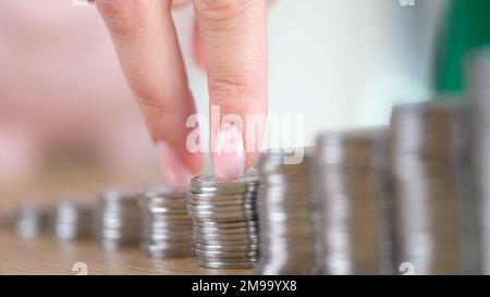 Nahaufnahme von weiblichen Fingern, die auf Münzstapeln auf einem Holztisch gehen. Stockfoto