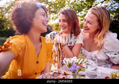 Drei Weibliche Freunde Sitzen Draußen Im Summer Garden At Home Und Essen Zusammen Stockfoto