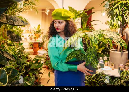 Junge Frau, die heimische grüne Pflanzen in einem Laden auswählt Stockfoto