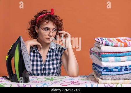 Ein Mädchen mit Brille blickt auf ein paar gebügelte Handtücher. Lockiges Haar. Stockfoto