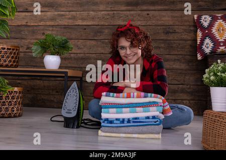 Das Mädchen sitzt auf dem Boden und lehnt sich auf frisch gewaschene und gebügelte Handtücher. Stockfoto