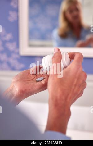 Nahaufnahme Einer Menopausalen Frau, Die Vitamine Oder Medikamente In Mirror At Home Einnimmt Stockfoto