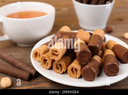 Teller mit köstlichen Waffeln mit Haselnüssen und einer Tasse Tee auf Holzhintergrund Stockfoto