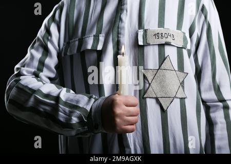 Jüdischer Gefangener mit Marke und brennender Kerze auf schwarzem Hintergrund, Nahaufnahme. Internationaler Holocaust-Gedenktag Stockfoto