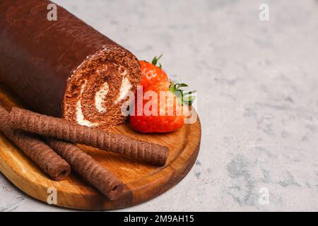 Holzbrett mit leckeren Kuchenrollen, Waffelrollen und Erdbeeren auf Grunge-Hintergrund, Nahaufnahme Stockfoto